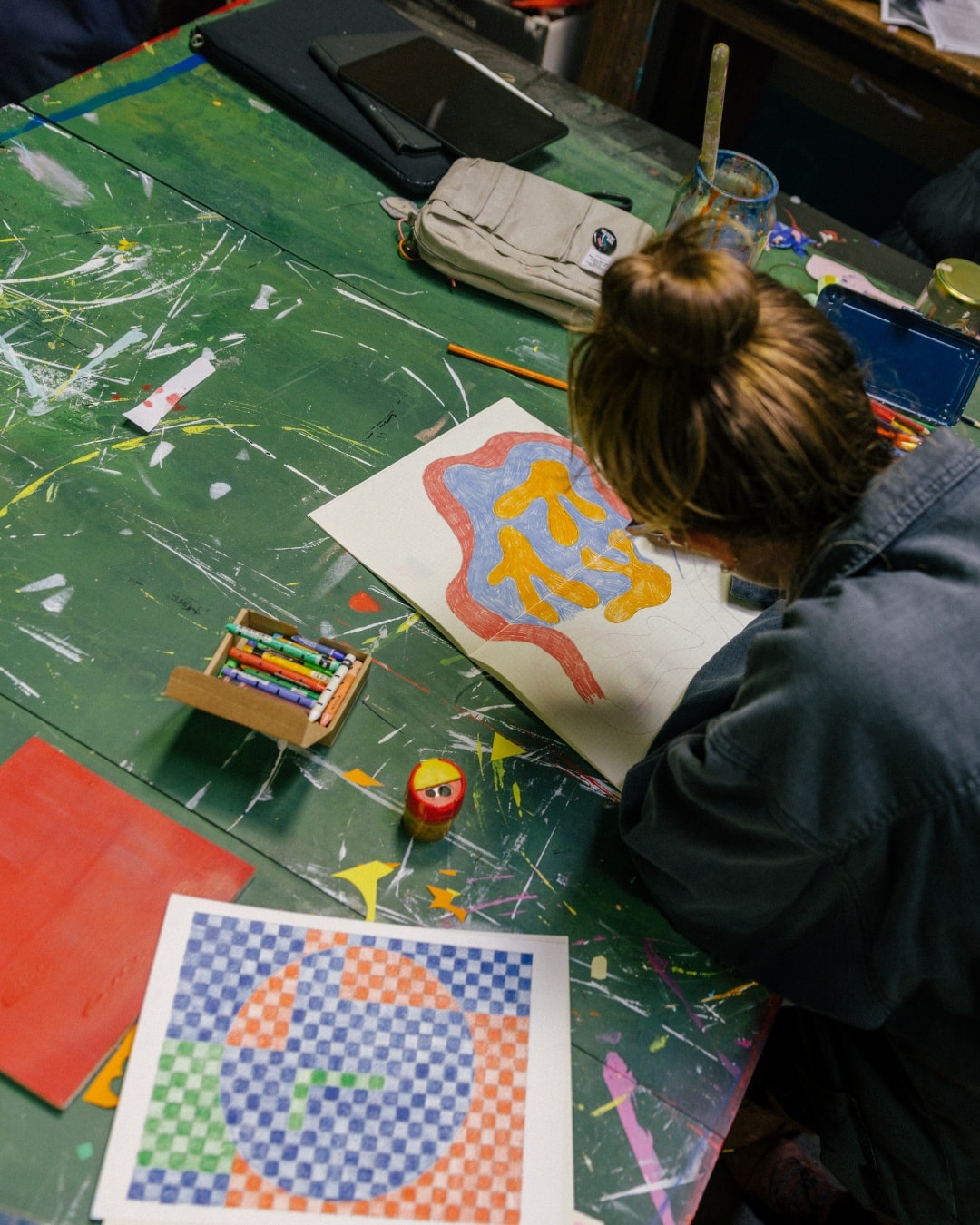 Abbey Rich from above, drawing a blue and yellow shape on paper at the paint-splattered table