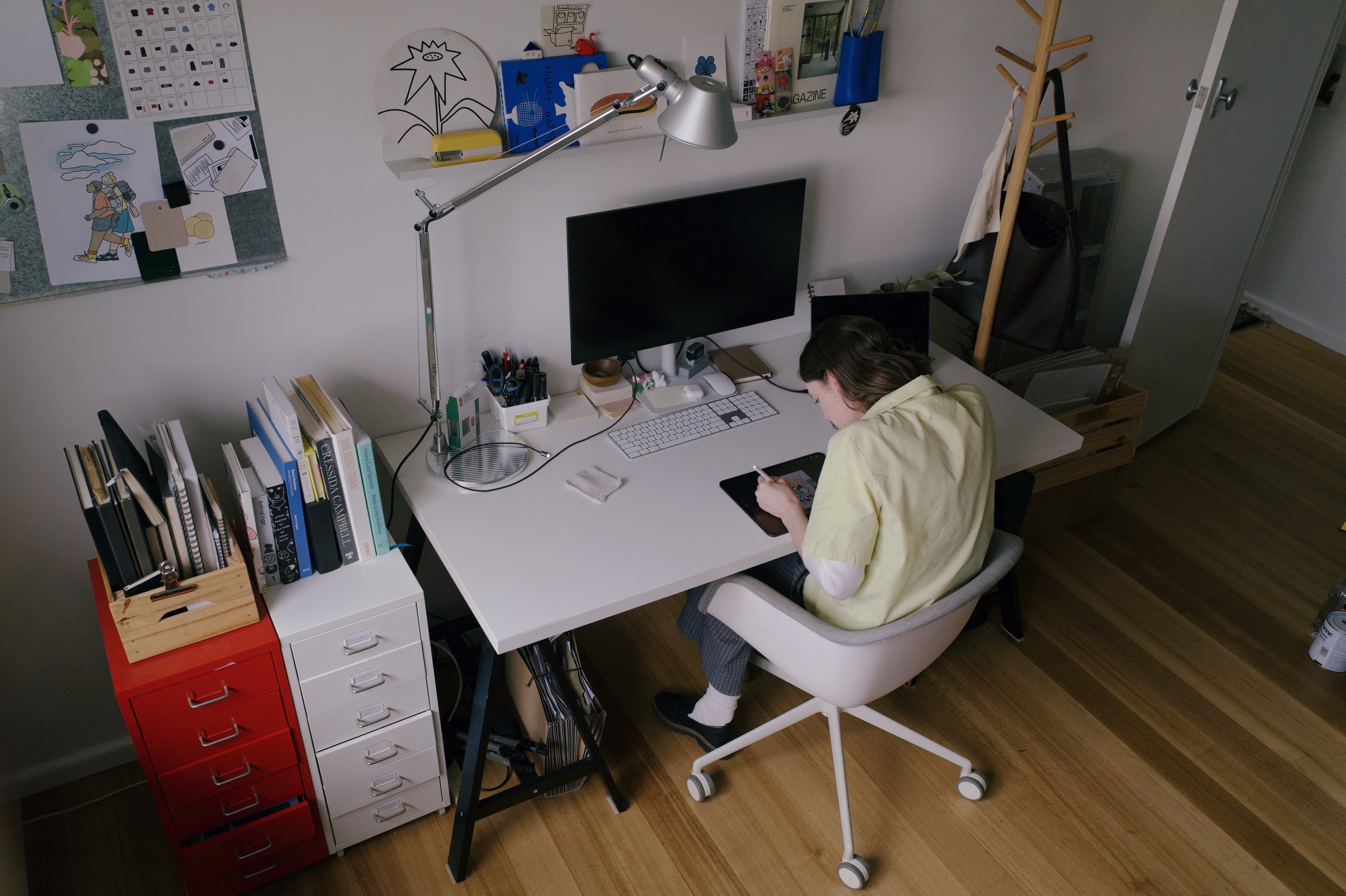 Angharad at her desk by the computer, a pinboard of drawings above her