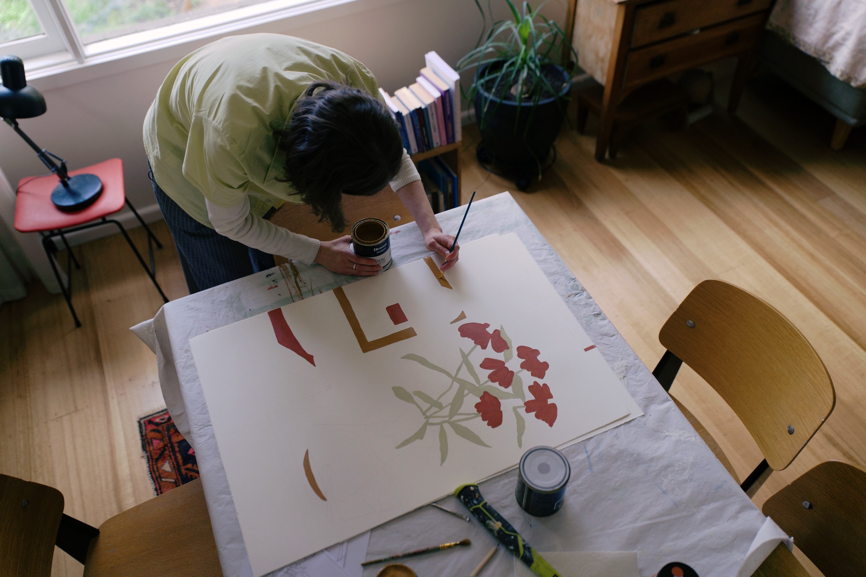 Angharad painting red flowers and flat orange shapes on a large sheet of paper