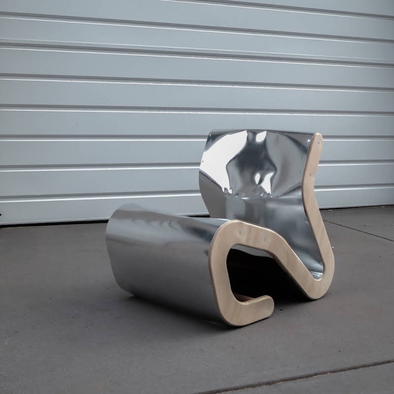 The finished chair, curved plywood skinned in polished aluminium, on the driveway