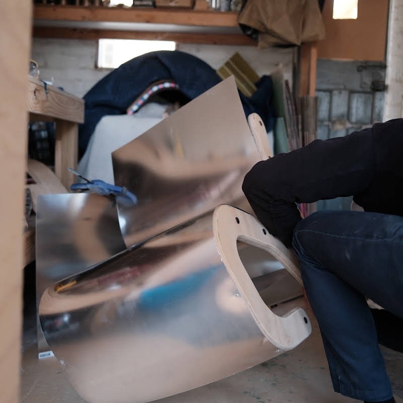 Billy bending a sheet of aluminium around the plywood frame of a chair