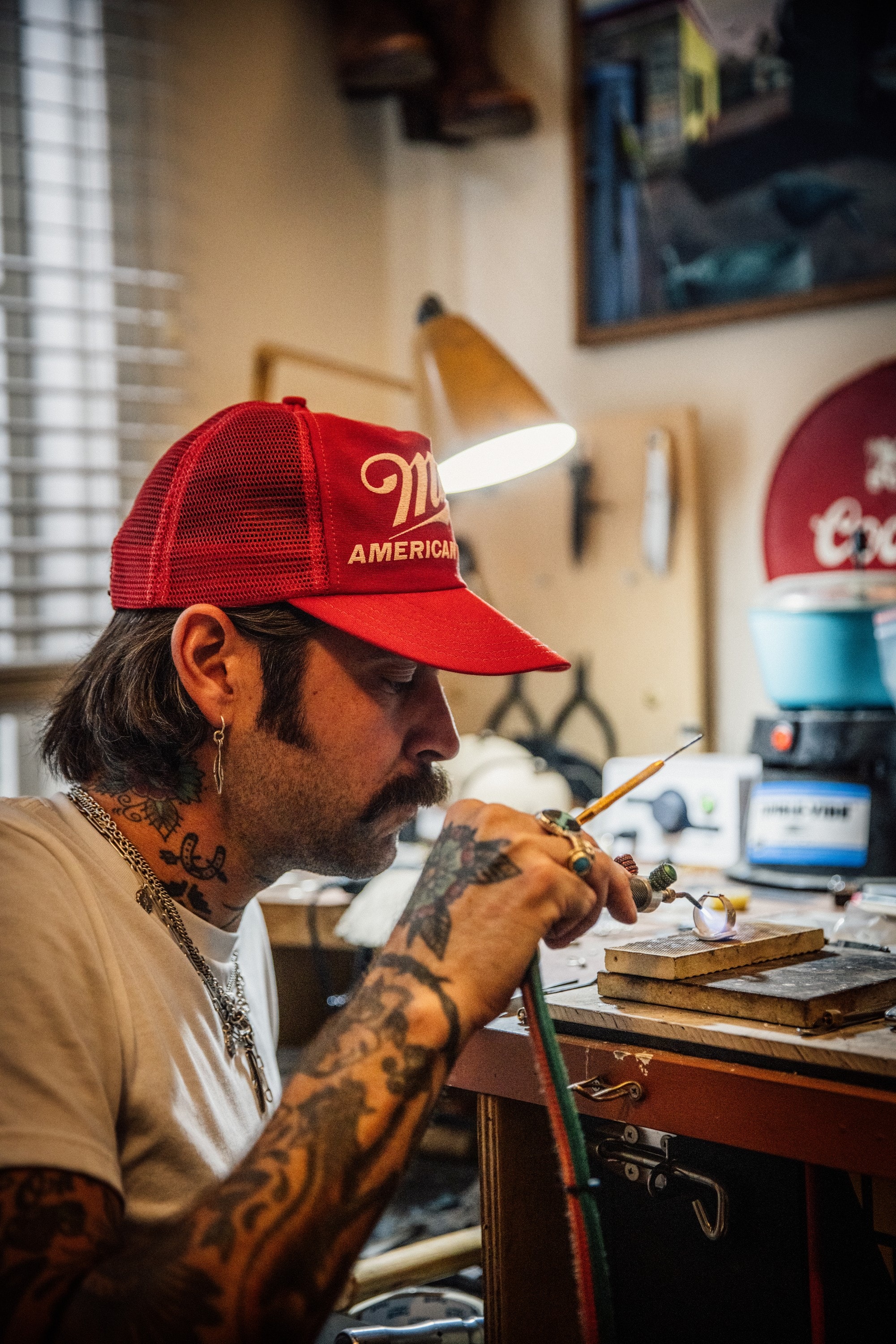 Adam soldering at the bench with a torch, a lamp angled over his work