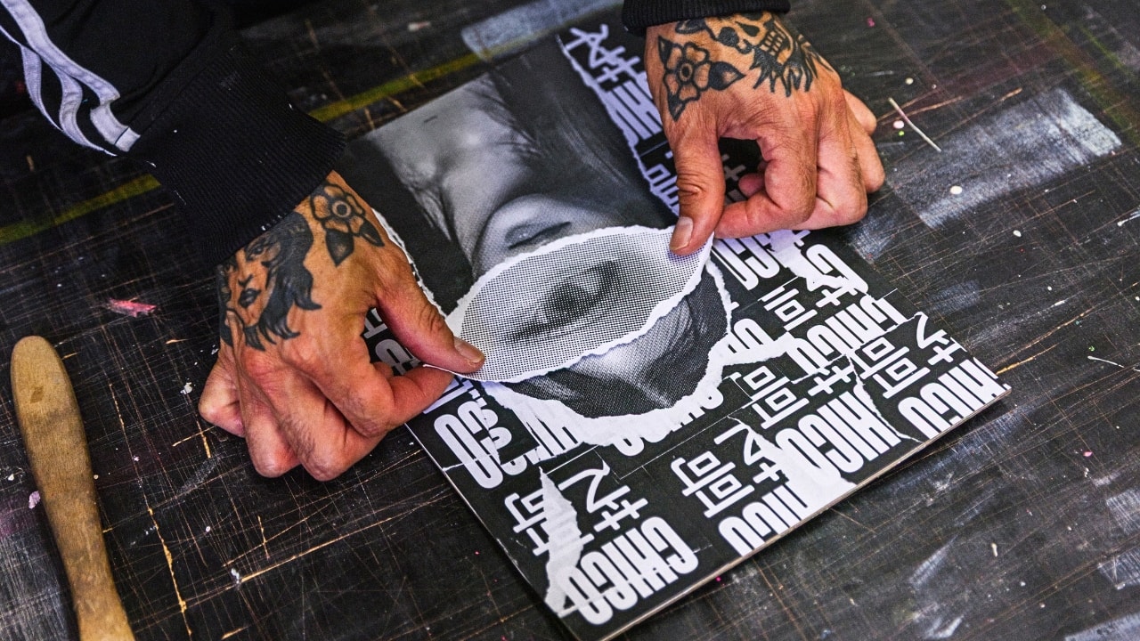 Chico Leong’s tattooed hands placing a torn cut-out eye onto a collage of black and white letters