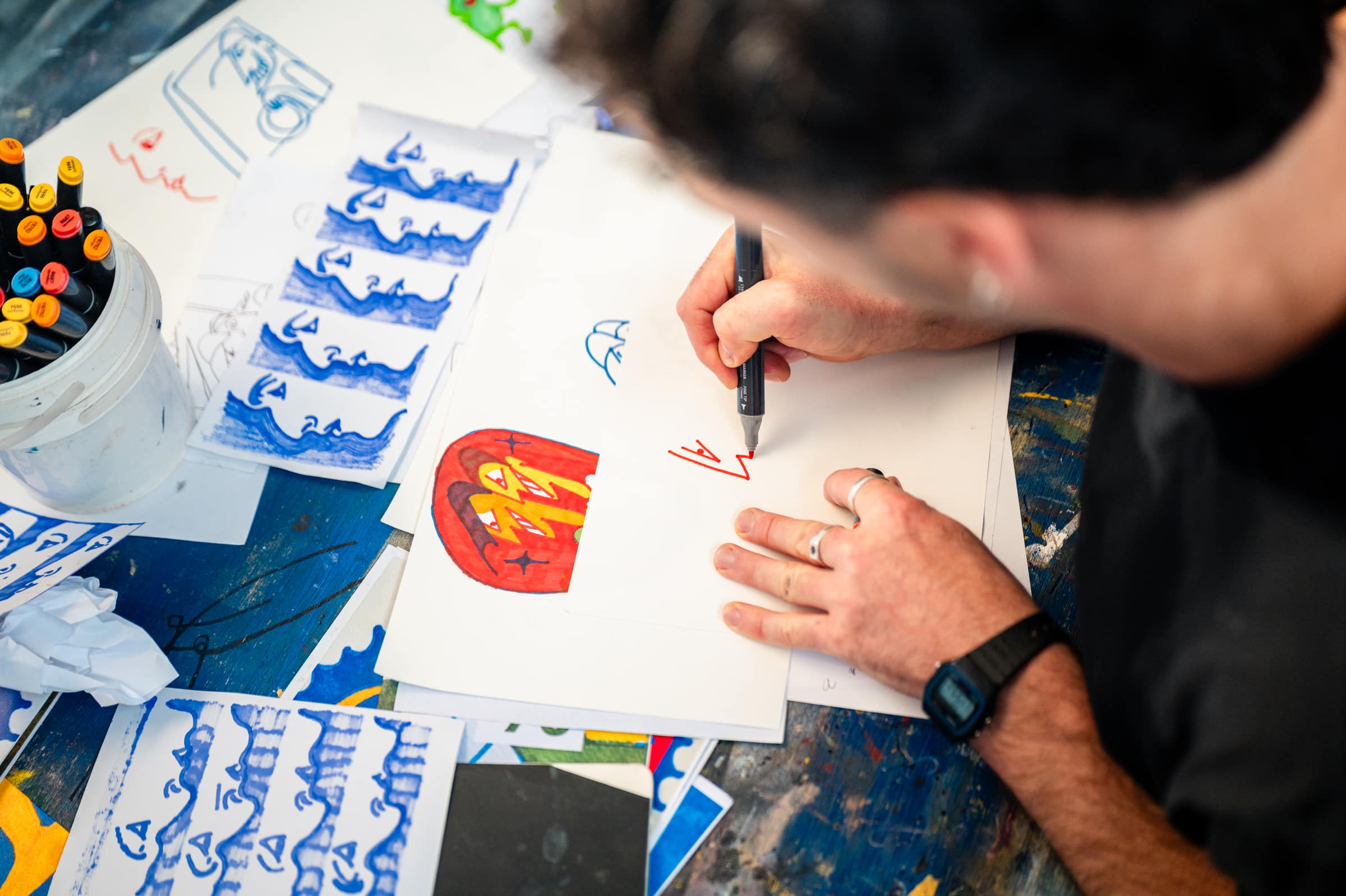 Chris’s hand drawing a red Commodore in texta, finished blue drawings around it
