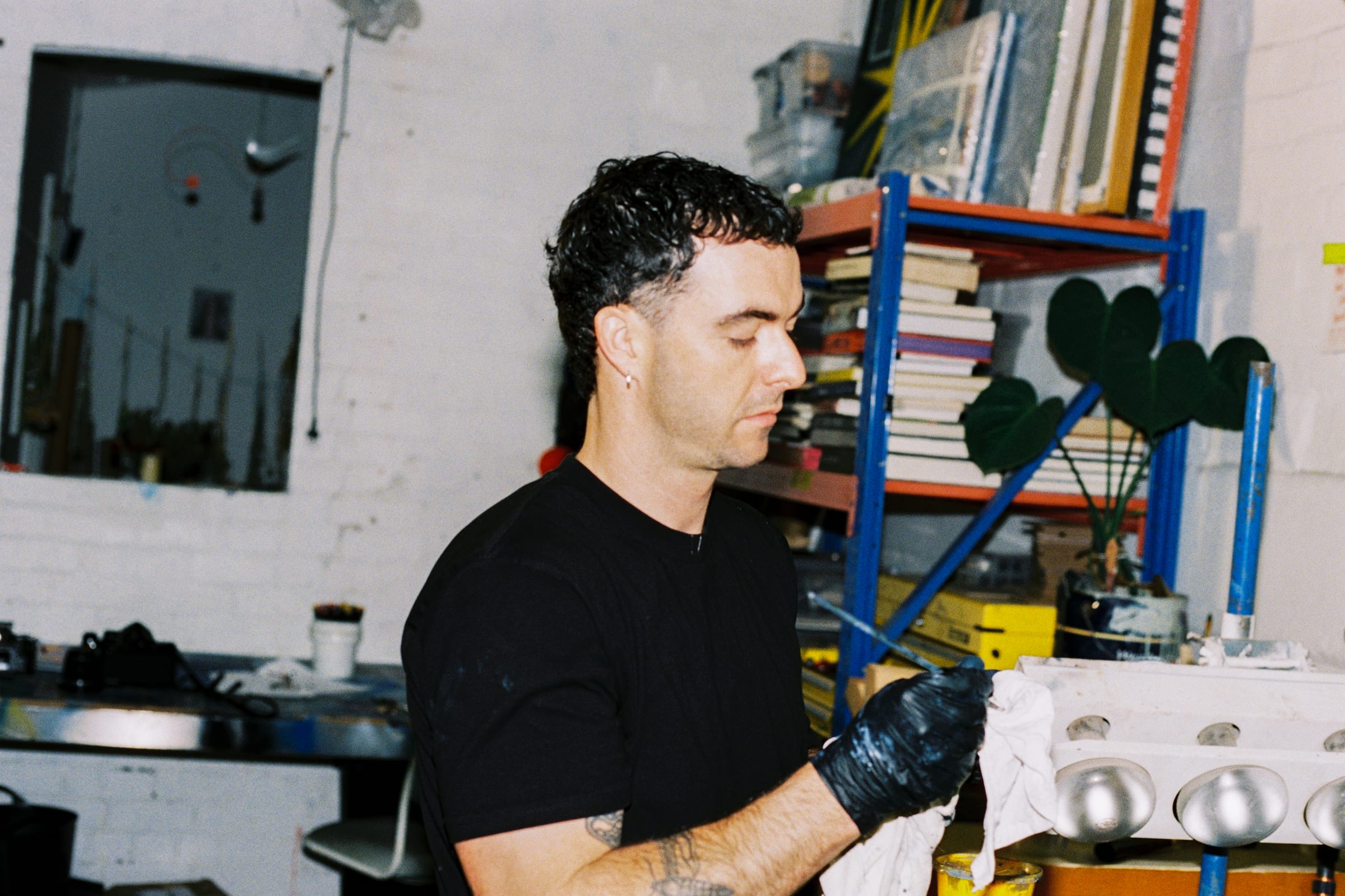 Chris in black gloves working on a canvas beside his studio shelves