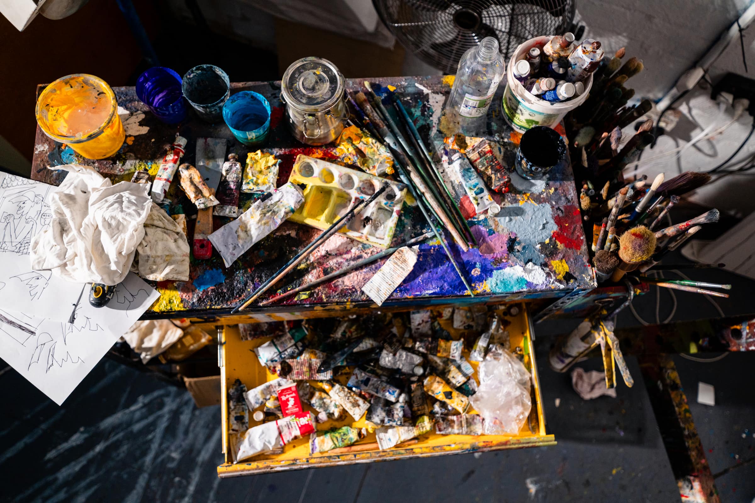 Looking down on a paint table crowded with tins, jars, brushes and rags