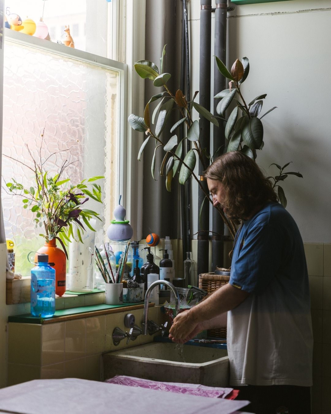 David Booth washing up at the studio sink beside a window full of plants