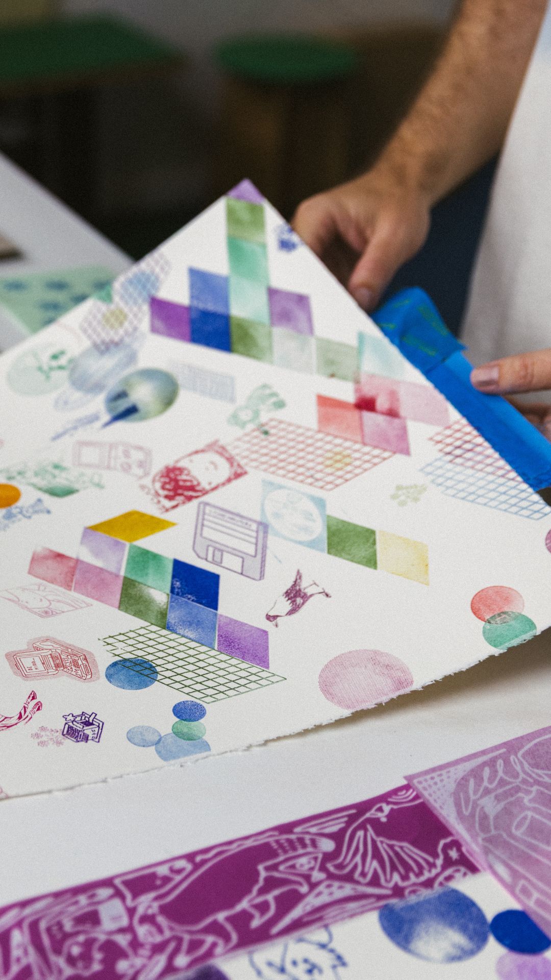 A stamped print on paper, layered with coloured diamonds, grids and small figures