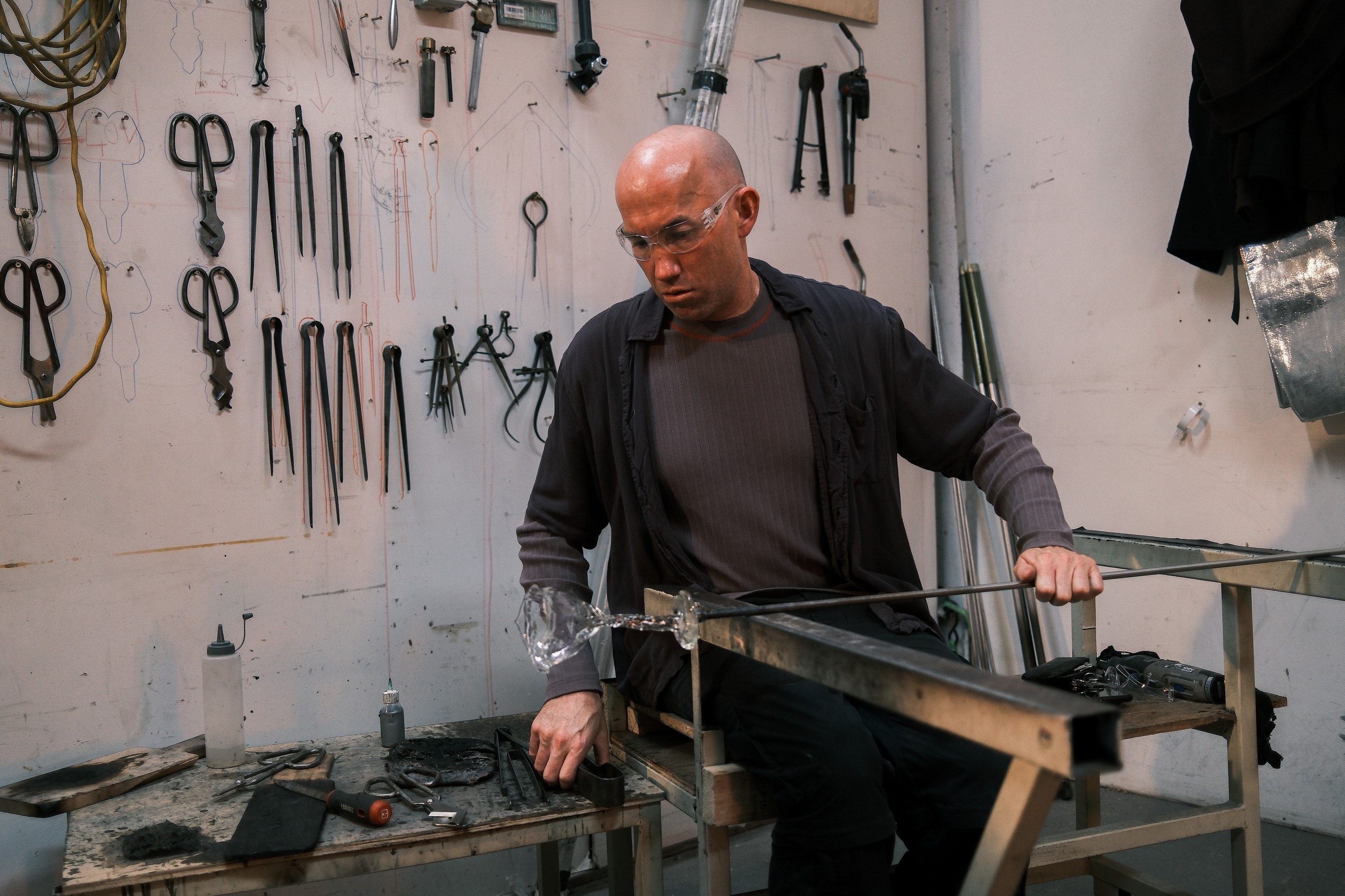 Billy shaping a piece at the bench, tools hanging on the wall behind him