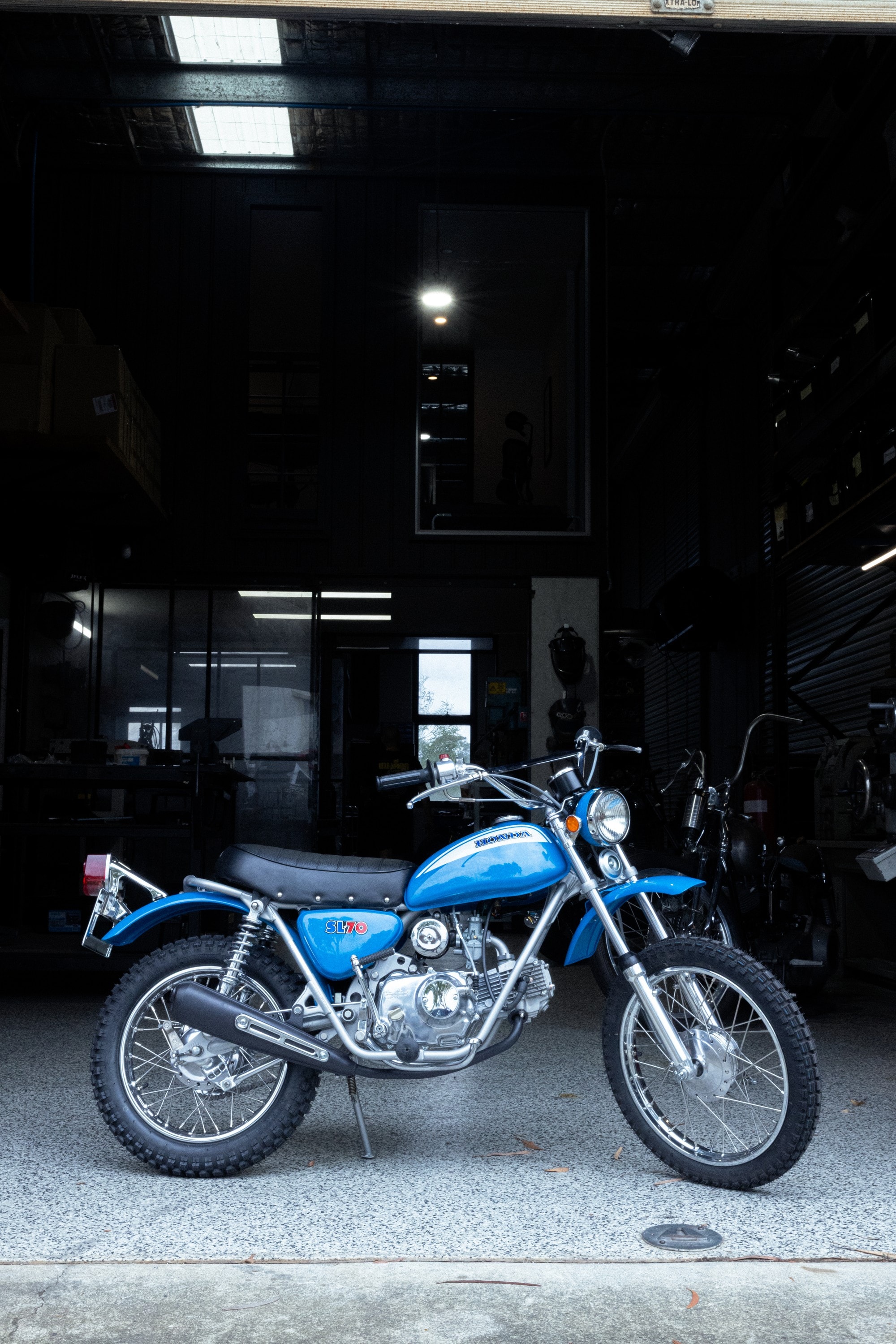 A blue motorcycle parked on the polished floor at the open door of Tom Gilroy’s workshop
