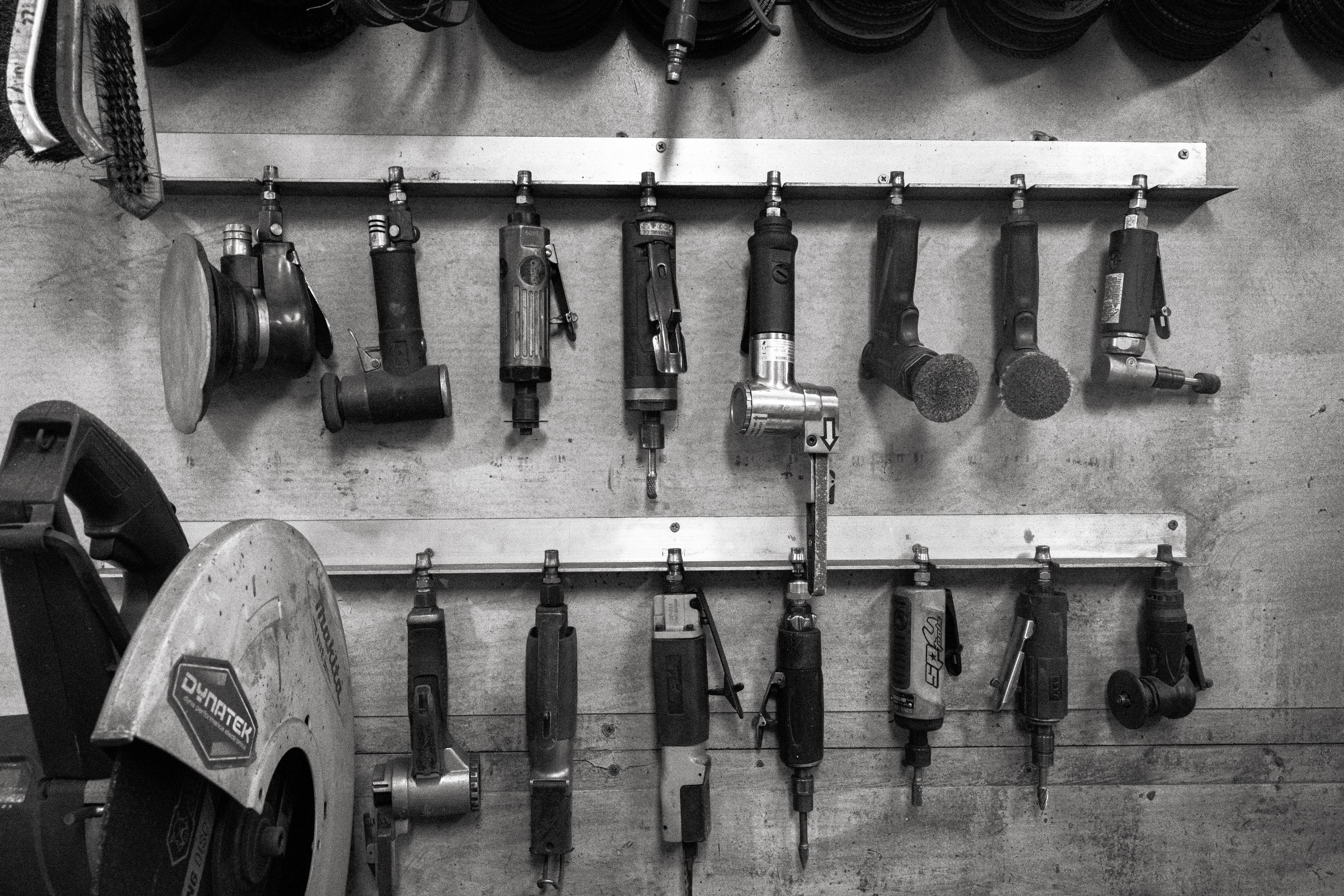Air tools hanging in two rows on the workshop wall beside a motorcycle fender