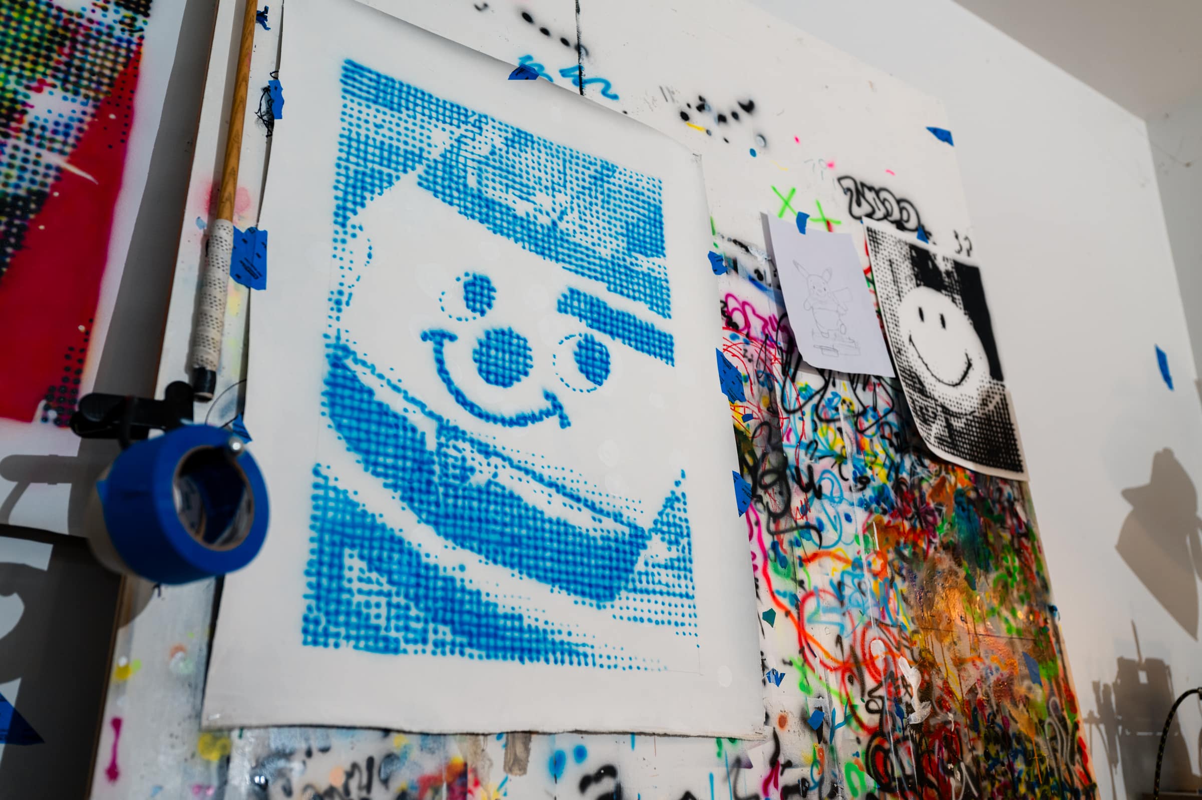 A blue halftone painting of a smiling clown face pinned to the wall