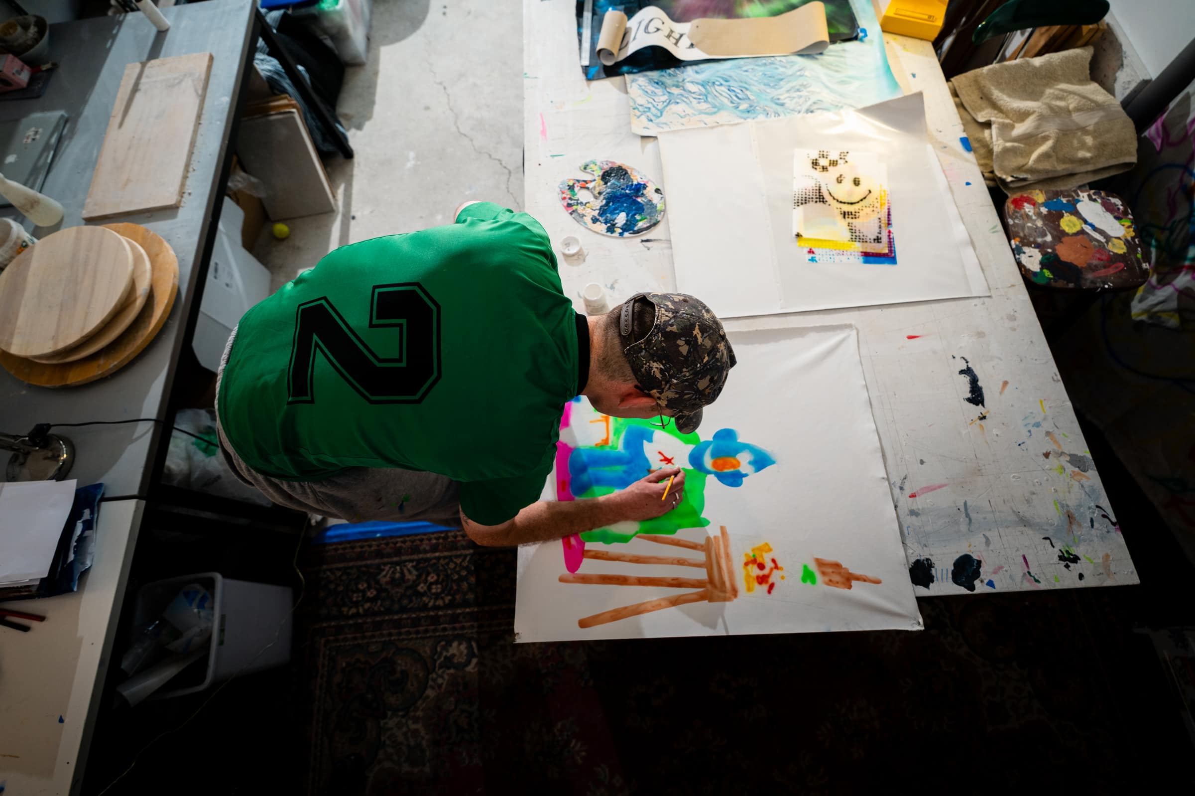 Overhead view of Liam leaning over a large fluoro painting laid flat on the table