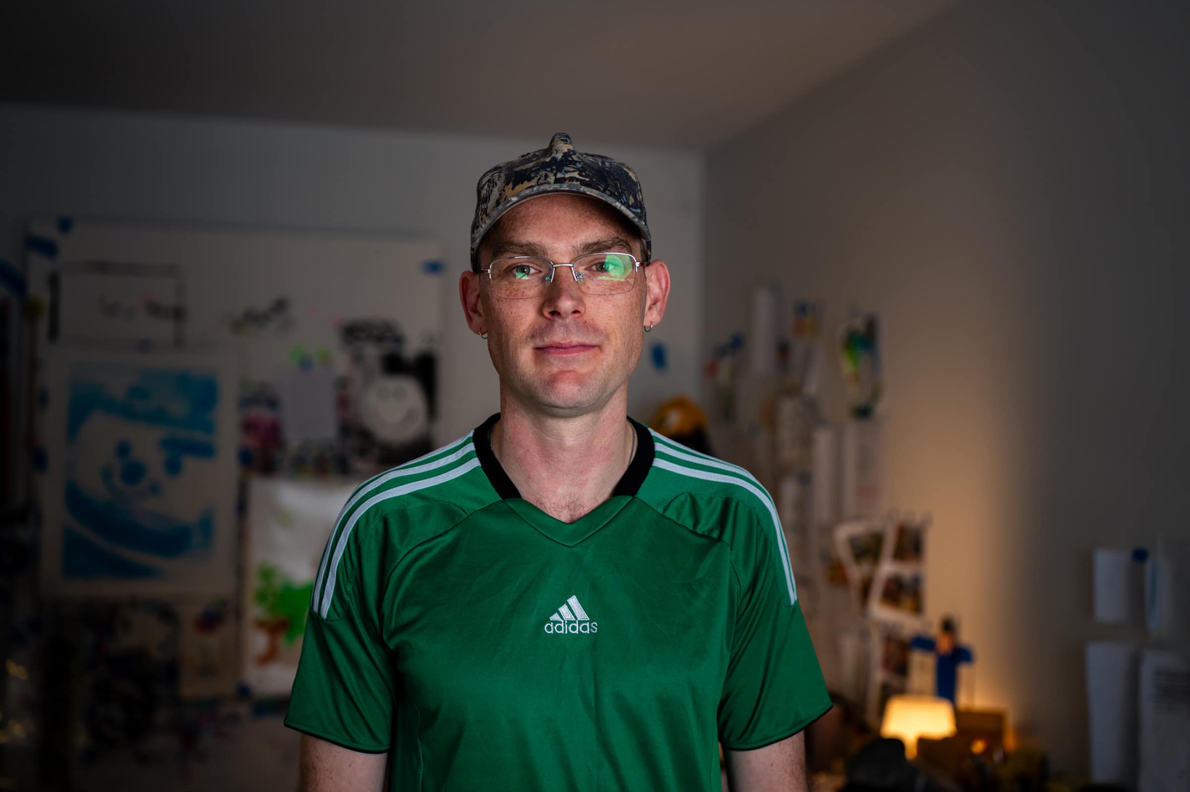Liam in a green football shirt and camo cap, standing in his studio