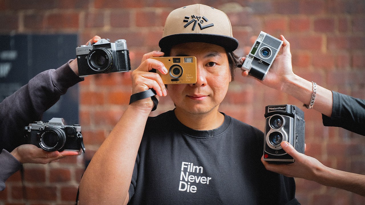 Gary Wong holding a gold Nana camera to his eye, surrounded by film cameras held out by other hands